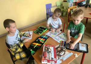 Nauka języka niemieckiego poprzez zabawę w świetlicy szkolnej. Uczniowie siedzą przy stole i kolorują pisakami karty pracy.